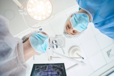 Foto de Cirujano dentista con un asistente están en el quirófano, la habitación es estéril y la luz - Imagen libre de derechos