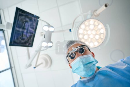 Foto de Hombre con lentes especiales y un uniforme médico trabaja en el quirófano, la habitación es ligera y estéril - Imagen libre de derechos