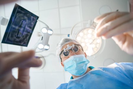 Foto de Cirujano dentista en lentes especiales está en el quirófano, la habitación es ligera y estéril - Imagen libre de derechos