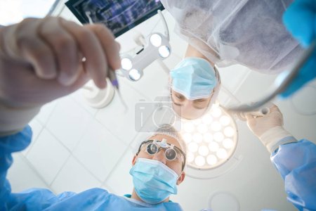 Foto de Cirujano dentista en lentes especiales en el lugar de trabajo en el quirófano, una asistente femenina le ayuda - Imagen libre de derechos