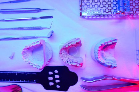 Téléchargez les photos : Moulages en plâtre de la mâchoire et des instruments dentaires spéciaux se trouvent sur la table, ils sont traités par une lampe infrarouge - en image libre de droit