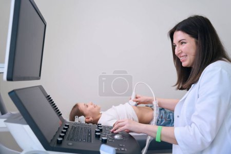 Foto de Médico benévolo realiza un ultrasonido de los órganos internos de una niña, una mujer con una bata médica - Imagen libre de derechos