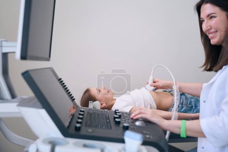 Foto de Lindo niño se encuentra en un sofá médico en una sala de ultrasonido, el médico realiza una ecografía de los órganos internos - Imagen libre de derechos