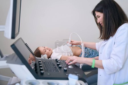 Foto de Médico mujer realiza una ecografía de los órganos internos de una niña, un diagnóstico en una bata médica - Imagen libre de derechos