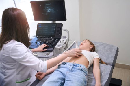Ärztin führt Ultraschall der inneren Organe eines kleinen Mädchens durch, der Diagnostiker blickt auf den Monitor