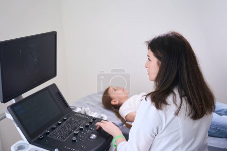 Photo for Calm girl lies on the couch in the ultrasound room, the doctor conducts an ultrasound of the internal organs - Royalty Free Image
