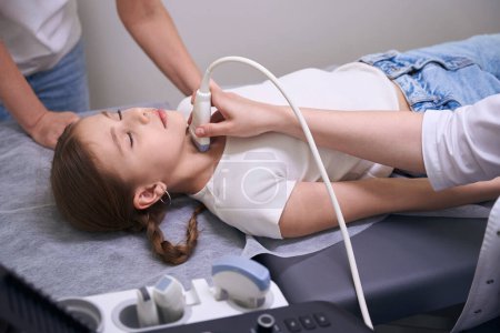 Girl with pigtails in the clinic for ultrasound of the thyroid gland, the diagnostician uses modern equipment