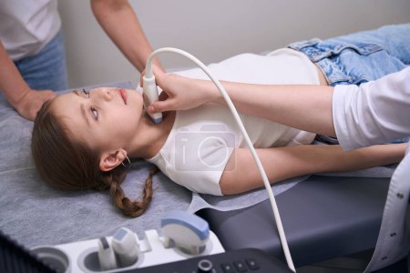 Téléchargez les photos : Jeune patient dans une clinique pour échographie de la glande thyroïde, le diagnosticien utilise un équipement moderne - en image libre de droit