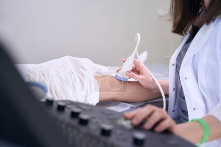 Foto de Diagnóstico mujer lleva a cabo un procedimiento de ultrasonido de la articulación de la rodilla pacientes, un especialista utiliza equipos modernos - Imagen libre de derechos