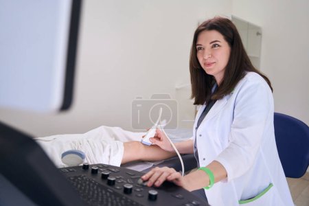 Foto de Mujer diagnosticador realiza un examen por ultrasonido de la articulación de la rodilla, la paciente se encuentra en un sofá médico - Imagen libre de derechos