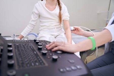 Foto de El especialista en ultrasonido lleva a cabo un examen de un niño en una máquina de ultrasonido, el médico trabaja con la articulación del codo - Imagen libre de derechos