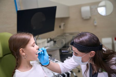 Foto de Otorrinolaringólogo especialista en guantes protectores examina la garganta de los niños, el médico utiliza herramientas especiales - Imagen libre de derechos
