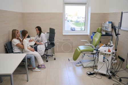 Foto de La otorrinolaringóloga se comunica con una pequeña paciente y su madre en un consultorio otorrinolaringológico, en interiores con equipo especial - Imagen libre de derechos