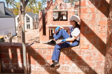 Foto de Ingeniera de construcción mujer descansando, sentada en el agujero de la ventana de la casa en construcción y mirando el proceso de construcción, desarrollo de viviendas - Imagen libre de derechos