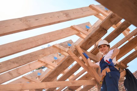 Photo for Confident woman builder checking quality of wooden roof construction installation, inspecting details, hammering some nails, forewoman responsible for construction site - Royalty Free Image