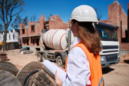 Photo for Female building engineer in hardhat controlling building process walking along construction site, housing development - Royalty Free Image