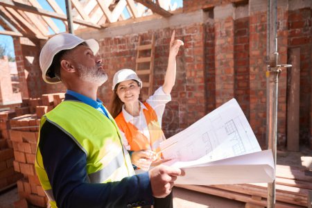 Photo for Building engineers in hardhats discussing roof construction looking at blueprint, roofer getting acquainted with the roof project - Royalty Free Image