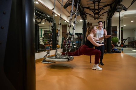 Foto de Entrenador de fitness apoya a una mujer cuando realiza un ejercicio de acuerdo con una técnica especial, ella utiliza una plataforma de suspensión especial - Imagen libre de derechos