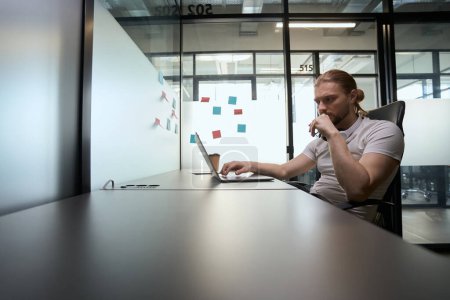 Foto de El hombre reflexivo se sienta en su escritorio delante de un ordenador portátil, pegatinas multicolores en una partición transparente - Imagen libre de derechos