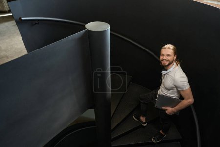 Téléchargez les photos : Heureux employé se tient sur les escaliers dans le hall de coworking, intérieur élégant - en image libre de droit