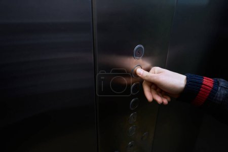 Téléchargez les photos : Homme dans la cabine de l'ascenseur de passagers appuie sur le bouton de sélection du sol, l'homme appuie sur le bouton avec son pouce - en image libre de droit