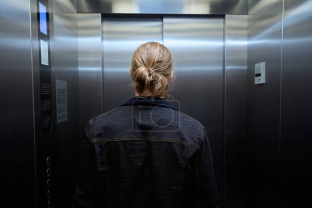 Hombre en una chaqueta de mezclilla está en la cabina del elevador de pasajeros, a la izquierda es el panel con botones de selección de piso