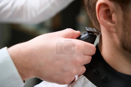Photo for Cropped view on hand of hairdresser trimming hair of visitor by using barber machine - Royalty Free Image