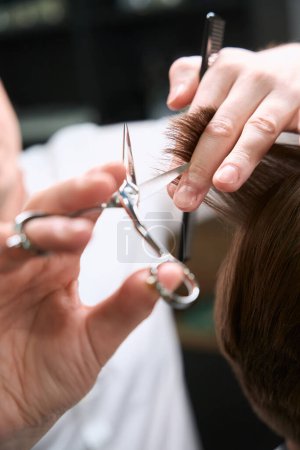 Téléchargez les photos : Vue rapprochée sur les mains du coiffeur faisant coiffure élégante pour son visiteur dans le salon moderne - en image libre de droit