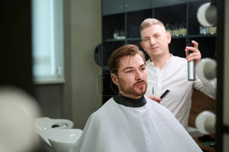 Photo for Skilled hair stylist wetting hair of his client by using spray in modern barbershop - Royalty Free Image