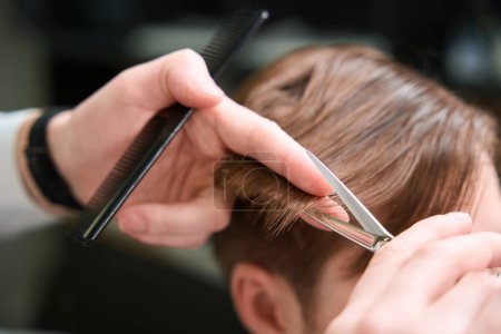 Foto de Vista de cerca en las manos de la peluquería haciendo corte de pelo elegante para el visitante en la barbería moderna - Imagen libre de derechos