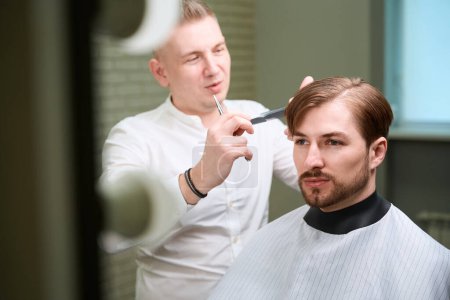 Photo for Male hairdresser creating new hair look to his client by using scissors and comb in modern room - Royalty Free Image