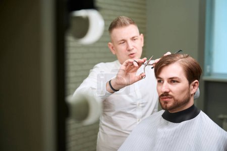 Photo for Young handsome man having trendy haircut from professional barber in modern salon room - Royalty Free Image