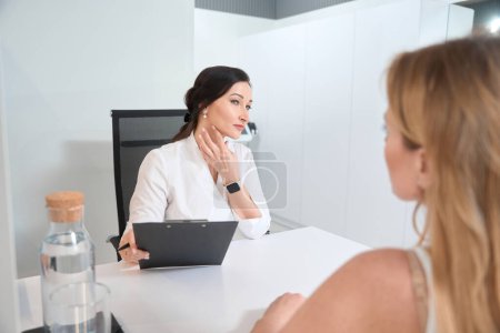 Photo for Female doctor consults a woman in a cosmetology clinic, she selects options for non-surgical skin tightening - Royalty Free Image