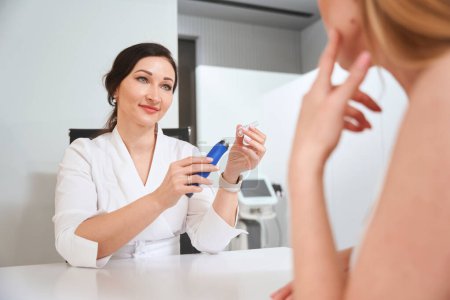 Téléchargez les photos : Esthéticienne spécialiste offre au client un produit de soins efficace, une femme sur une consultation dans une clinique de cosmétologie - en image libre de droit