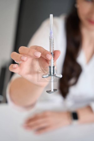 Photo for Specialist cosmetologist demonstrates a syringe with a rejuvenating substance, she has a smart watch on her hand - Royalty Free Image
