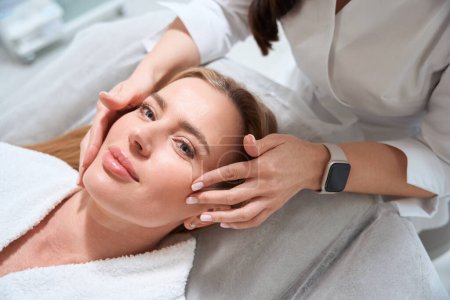 Photo for Female masseuse makes a professional facial massage to a patient, the woman has a smart watch - Royalty Free Image
