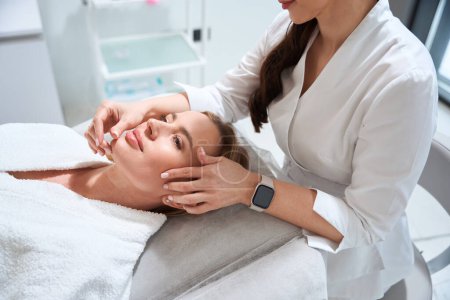 Photo for Female masseuse at the workplace makes a professional massage to a patient, a specialist works with a womans face - Royalty Free Image