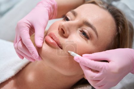Foto de Mujer rubia en una consulta en una clínica de cosmetología, un especialista utiliza un marcador especial para marcar las áreas de trabajo - Imagen libre de derechos