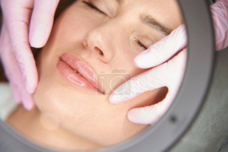 Téléchargez les photos : Esthéticienne examine les plis nasolabiaux du patient après des injections de beauté, spécialiste utilise une loupe - en image libre de droit