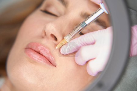 Photo for Esthetician makes injections to the woman in the nasolabial fold, the specialist uses a magnifying glass - Royalty Free Image