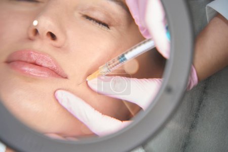 Photo for Woman on injection procedure in aesthetic medicine clinic, specialist uses magnifying glass - Royalty Free Image