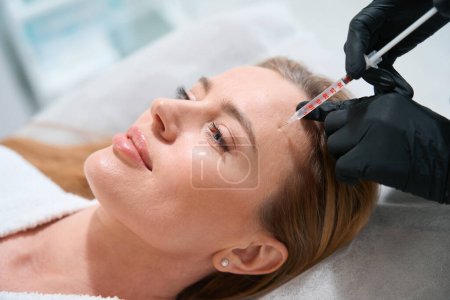 Foto de Mujer hermosa en un procedimiento de inyección en una clínica de medicina estética, un especialista utiliza una aguja delgada - Imagen libre de derechos