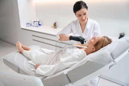 Der Mitarbeiter einer modernen Kosmetologie-Klinik spritzt eine Schönheitsspritze, die Patientin liegt auf einem speziellen Sofa