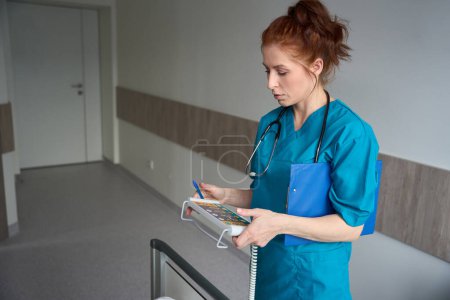 Photo for Female healthcare professional fine-tuning the remote monitoring control panel of the electronically adaptable bed in hospital room - Royalty Free Image