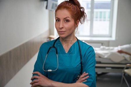 Téléchargez les photos : Portrait d'une femme médecin en uniforme avec les bras croisés debout dans la salle d'hôpital - en image libre de droit
