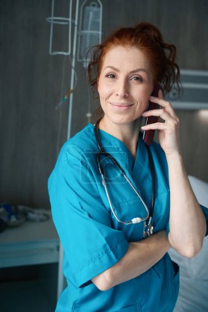 Photo for Smiling female nurse in uniform communicating through telephone in the hospital ward - Royalty Free Image