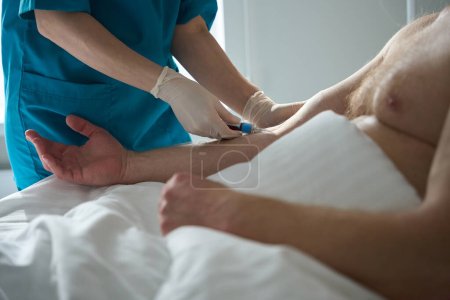Téléchargez les photos : Photo recadrée des mains de l'infirmière dans des gants en caoutchouc faisant une analyse de sang des patients veine en salle à la clinique - en image libre de droit