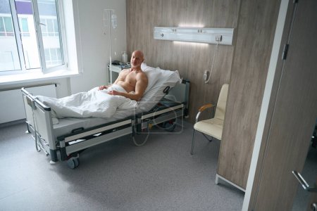 Foto de Paciente masculino hospitalizado acostado en la cama después de procedimientos médicos y esperando al médico en la cámara moderna en la clínica - Imagen libre de derechos
