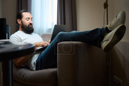 Téléchargez les photos : Homme d'âge moyen passe la soirée dans la communication en ligne, il est assis sur un canapé doux - en image libre de droit