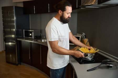 Foto de Hombre en ropa casual cocinar espaguetis, él está en el área de la cocina de la habitación del hotel - Imagen libre de derechos
